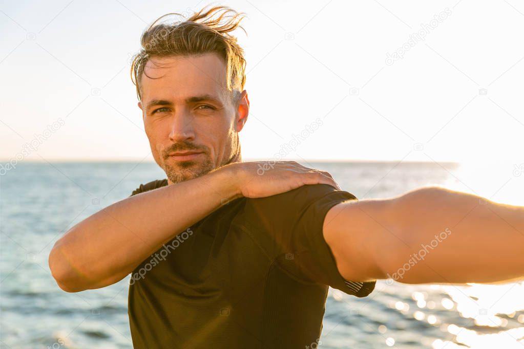 athletic adult man stretching arm before training on seashore