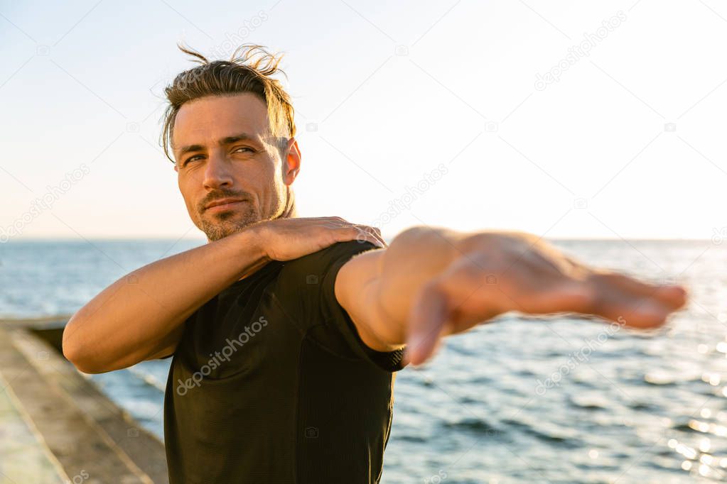 adult sportsman stretching arm before training on seashore