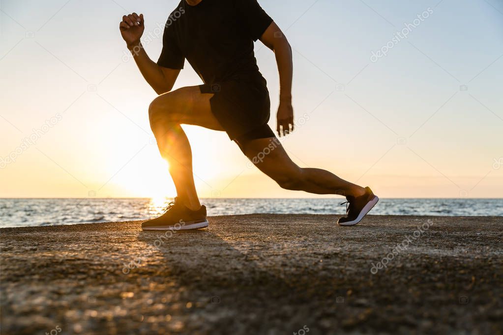 cropped shot of athletic man doing lunges during training on seashore