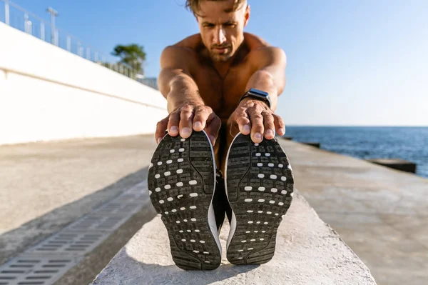Close-up shot of adult shirtless sportsman stretching before training on seashore — Stock Photo