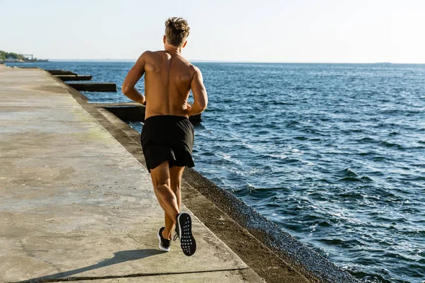 Rückansicht des muskulösen, hemdlosen Sportlers beim Joggen am Strand — Stockfoto