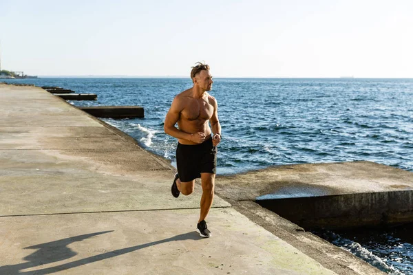 Beau adulte torse nu homme jogging sur le bord de la mer — Photo de stock