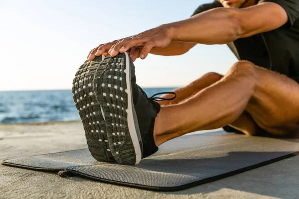 Cropped shot of athletic man stretching on seashore — Stock Photo