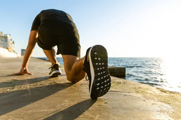 Atletico corridore sprint in posizione di partenza per corsa in riva al mare — Foto stock