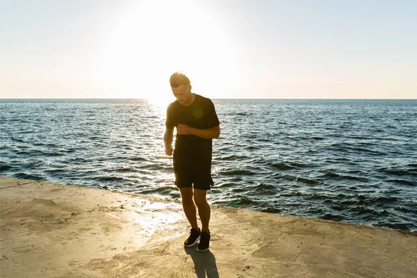 Handsome adult sportsman working out on seashore in front of sunrise — Stock Photo