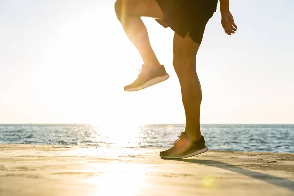 Cropped shot of sportsman working out on seashore in front of sunrise — Stock Photo