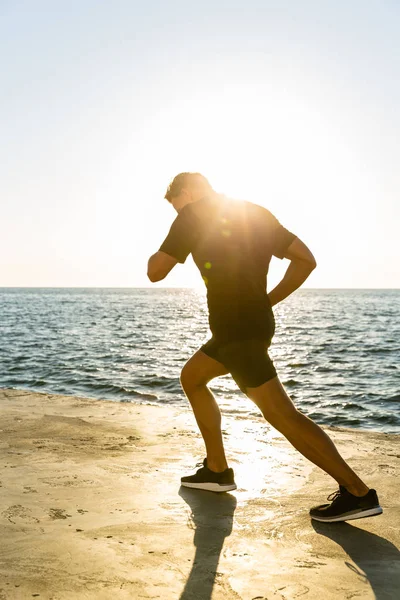 Sportif adulte faisant du jogging au bord de la mer devant le lever du soleil — Photo de stock