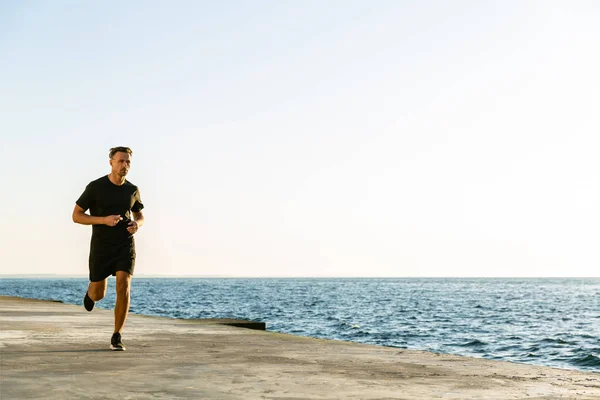 Handsome adult sportsman jogging on seashore in morning — Stock Photo