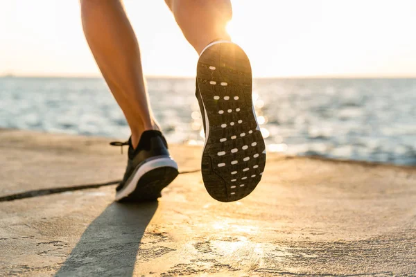 Cropped shot of sportsman in sneakers running by seashore on senrise — Stock Photo