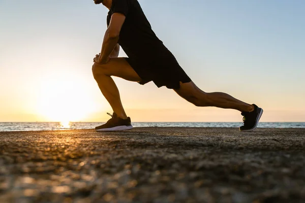 Cropped shot of sportsman doing lunges during training on seashore — Stock Photo