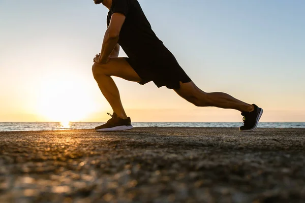 Colpo ritagliato di sportivo che fa affondi durante l'allenamento in riva al mare — Foto stock