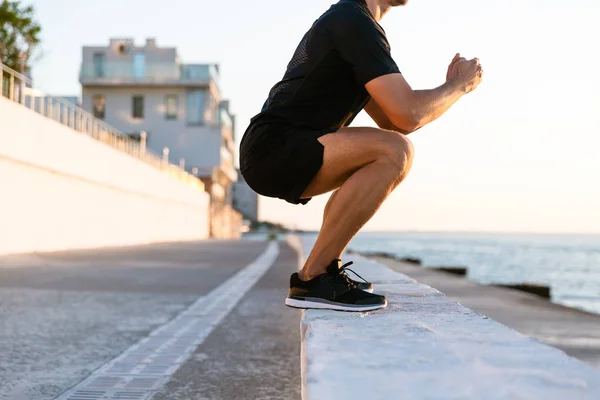 Обрізаний знімок спортсмена стоїть присідання на парапеті на березі моря — стокове фото