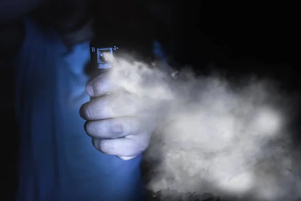 Una mano de hombre sostiene un gas pimienta aerosol en la oscuridad, un respaldo negro — Foto de Stock