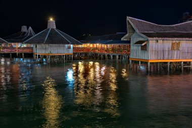 Semporna. Malezya. 29 Kasım 2018. Borneo kıyısındaki ayaklıklar üzerindeki deniz oteli akşam ışıklarıyla aydınlatılıyor. Karanlığın erken başlaması turistlerin gece geç saatlere kadar dinlenmesini engellemez..