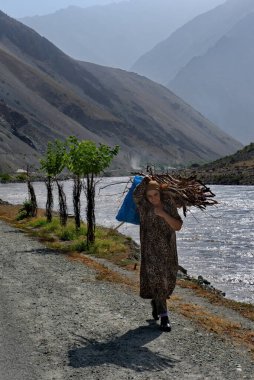 Ishkashim. Tacikistan. 08 Ağustos 2019. Bir dağ köyünden yaşlı bir kadın Pamir otoyolu boyunca omuzlarında yakacak odun yığını taşıyor..