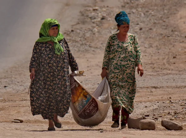 Nurek. Tacikistan. 07 Ağustos 2019. Ulusal giysili kadınlar şehrin sokaklarını elle süpürüp çöpleri topluyorlar. Geleneksel olarak, bunu sadece kadınlar yapar..