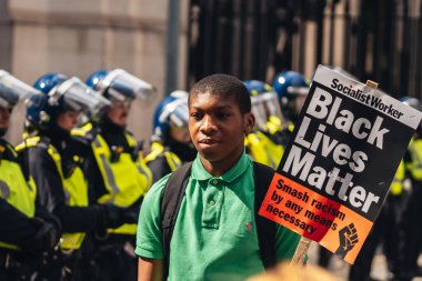 Londra / İngiltere - 06 / 13 / 2020: Siyahi Yaşamı Önemlidir protestosu koronavirüs salgını sırasında. Polis memurlarının önünde BLM bayrağı taşıyan genç adam.