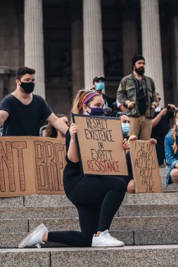Londra / İngiltere - 06 / 13 / 2020: Siyahi Yaşamı Önemlidir protestosu koronavirüs salgını sırasında. Trafalgar Meydanı 'nda bayraklı genç beyaz kız diz çöküyor.