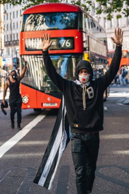 Londra / İngiltere - 06 / 13 / 2020: Siyahi Yaşamı Önemlidir protestosu koronavirüs salgını sırasında. Amerikan bayrağı pelerinli bir adam otobüsün önünde elleri havada yürüyor.
