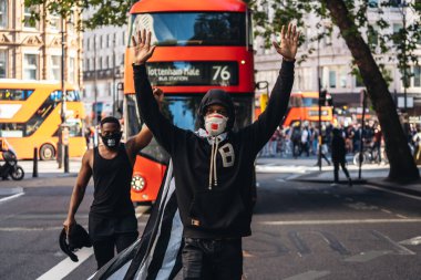 Londra / İngiltere - 06 / 13 / 2020: Siyahi Yaşamı Önemlidir protestosu koronavirüs salgını sırasında. Amerikan bayrağı pelerinli bir adam otobüsün önünde elleri havada yürüyor.