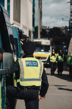 Londra, Birleşik Krallık 2025.09.13 POLİS olarak işaretlenmiş yüksek görünür yelek giyen bir polis memuru konuşma özgürlüğü protestosu sırasında güzergahı izlerken ve emniyete alırken isyan minibüslerinin yanında duruyor. 