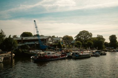Twickenham, Londra, Birleşik Krallık 2025.09.06 Thames Nehri 'nde büyük mavi bir vinç, demirli tekneler ve ağaçlarla çevrili nehir kenarındaki binaların görüntüsü.. 