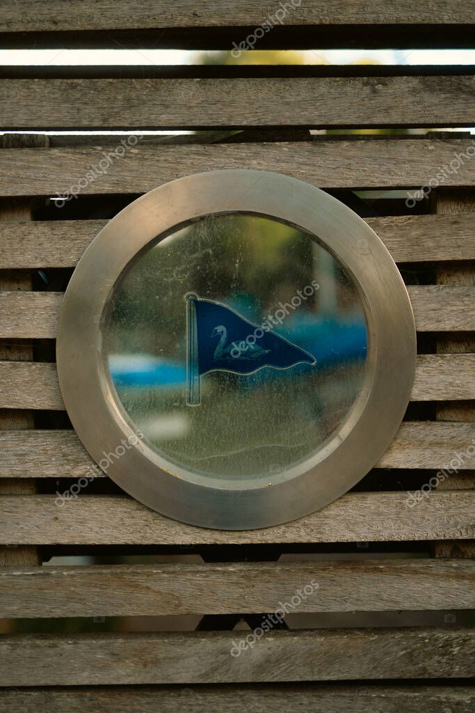 London, UK  2025.09.06  A circular metal plaque with a blue flag and swan emblem mounted on a wooden slatted bench, photographed during a walk in Twickenham Richmond