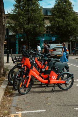 Chiswick, Londra, Birleşik Krallık 2025.08.14 Parlak turuncu Voi elektrikli bisikletleri işlek bir caddedeki rıhtım istasyonuna park etmiş, arka planda yayalar ve arabalar var.. 
