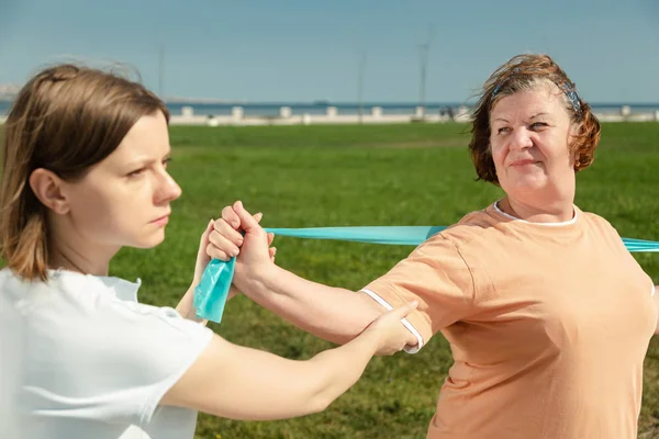 Une jeune formatrice aide une femme âgée à faire des exercices d'étirement. — Photo