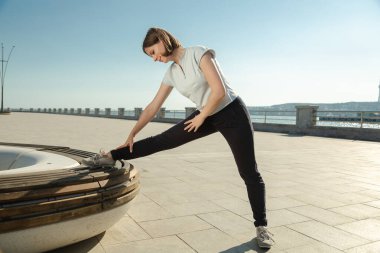 Genç bir kadın dışarıda yedek kulübesinde spor yapıyor..