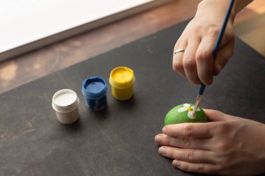 Paskalya yumurtalarını hazırlamak için yumurtanın üzerinde suluboya boyayla resim yapan kadın. Paskalya için ev yapımı dekorasyon.