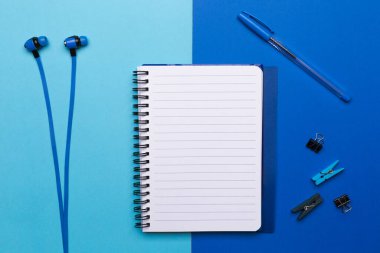 Mavi arka planda kalem ve kulaklık olan boş bir defter..