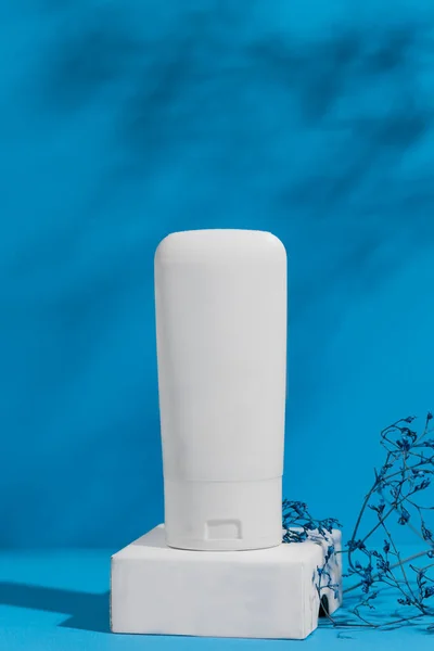 Tubo blanco del producto del cuidado de la piel en fondo azul, anuncio. Recipiente de tratamiento de la piel corporal con lugar para marca. Imagen de stock
