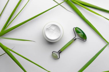 Yüze nemlendirici krem, beyaz arka planda yeşil yapraklı yeşim masaj aleti, ameliyat olmadan sağlıklı yaşam biçimi kavramı. Metin için kopyalama alanı olan cilt bakımı.