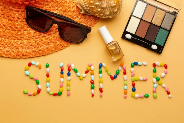 Słowo lato napisane kolorowe cukierki na pomarańczowym tle z okularami przeciwsłonecznymi i letni kapelusz na wybrzeżu. — Zdjęcie stockowe