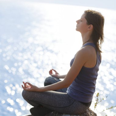 Genç bir kadın deniz kenarındaki kayalıklarda meditasyon yapıyor. Denizin kıyısında yoga egzersizi..