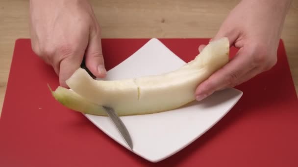 Чоловік нарізає диню на білій тарілці кухонним ножем, порція, щоб з'їсти солодкий десерт . — стокове відео