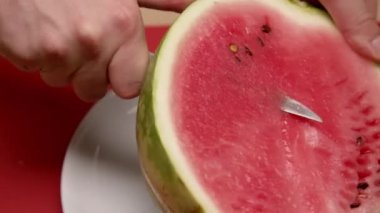 İnsanlar beyaz tabakta karpuz dilimliyor mutfak bıçağıyla, tatlı yemek için porsiyon..