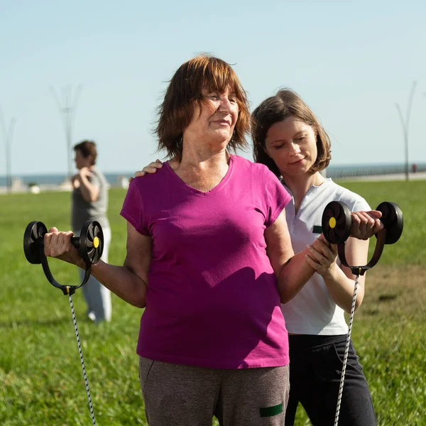 Mujer joven entrenador ayuda a la mujer mayor haciendo ejercicios de estiramiento. — Foto de Stock