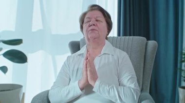 Kıdemli kadın koltukta meditasyon yapıyor, sakinleşmeye çalışıyor ve ilaç kullanmıyor. Yaşlı akrabaları için evinde tek başına dua ediyor. Yüksek kalite fotoğraf