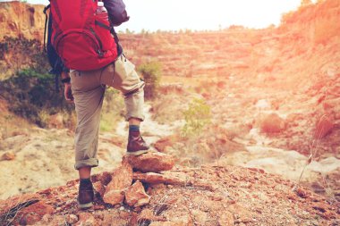 Dağın zirvesindeki kayalıkta genç adam sırt çantası yürüyüşçü bacaklar.