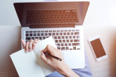 Üst görünüm ve dizüstü bilgisayar ve telefon kullanarak kadınların ellerini kapat. Proje hesap giderleri kavramı üzerine yaz ve eve çalışmayı kaydet.