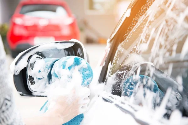 Female hand with blue sponge clean washing car side mirror. concept car wash.