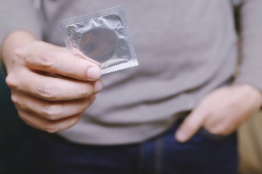 Prezervatif genç adam elinde kullanmaya hazır, yatakta prezervatif güvenli seks konsepti vermek Enfeksiyon önlemek ve Kontraseptifler doğum oranı veya güvenli profilaktik kontrol. Dünya Aids Günü, Metin için yer bırak.