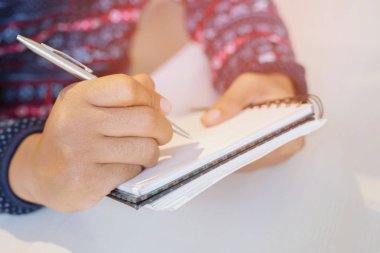 yakın el genç adam masa ahşap kitap içine Kayıt Anlatım günlük not defteri yazma kalem kullanarak oturuyor.
