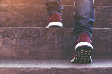 Merdiven. Yakın bacaklar kot pantolon ve ayakkabı spor ayakkabıları genç hipster adam kırmızı Bir kişi modern şehirde merdivenlerden yukarı çıkarken adım yürüyüş, merdiven, başarı, büyümek. Sabah güneş ışığı.