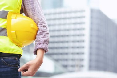 Mühendislik erkek inşaat işçisi standı nın arka görünümüne yakın iş çalışmasının güvenliği için güvenlik sarı kask tutarak. bina arka plan açık.