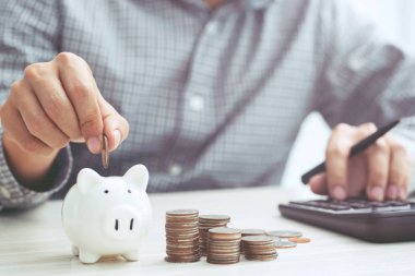 Hesap makinesi masraflarını hesaplayan el işi adamı. Tasarruf paralarını sıraya dizip, bozuk paraları kumbaraya koyan adam. kavram Yazı Finans Hesapları.