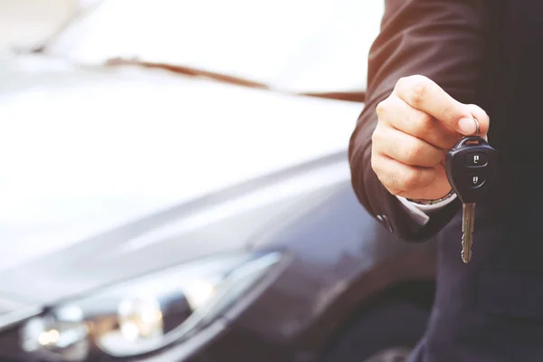 Business man hand holding car keys front with car on background. transport dealership and sales concept