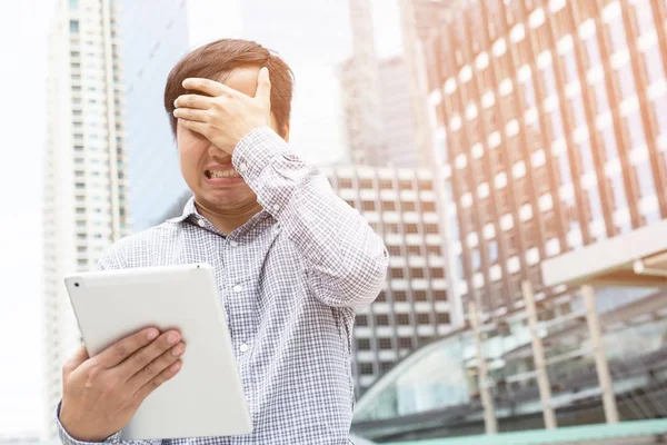 Yatırımcı genç işadamı dizüstü bilgisayar tableti kullanıyor. İş bağlantıları başarısız oldu. Ellerinizi yüzünüze koyun. Duygusal olarak çok üzgünüz..